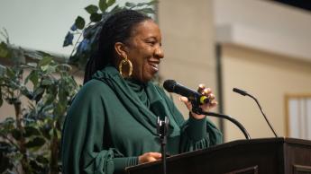 Tarana Burke speaking at a podium in a Cal Poly auditorium