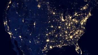 An aerial view of the United States at night with major cities illuminated with light