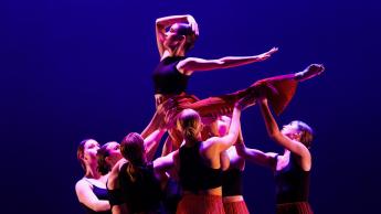 A group of dancers perform a lift on stage under blue lights