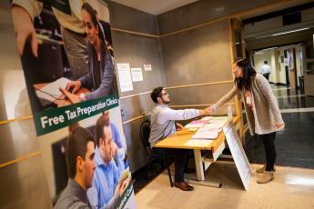 A student at a desk in the Volunteer Income Tax Assistance area shakes hands with a community member who has come in to get their taxes done.