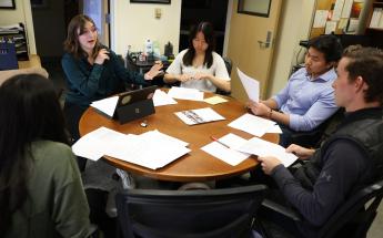 Five business students participating in the Low Income Taxpayer Clinic sit in conversation around a round table with papers in front of them.