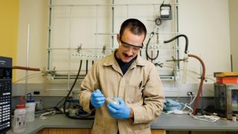 Chemistry student Sal Deguara wears a protective coat, gloves and glasses as he examines a compound in professor Scott Eagon's lab.