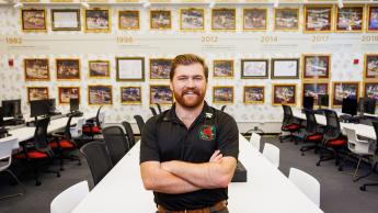 A student in a black Rose Float polo stands in a computer lounge decorated with Rose Float photos