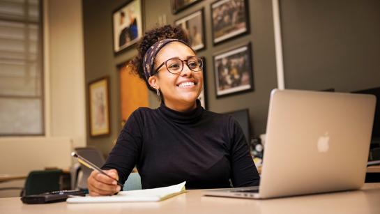 A Cal Poly student smiles broadly during her internship while sitting at her computer