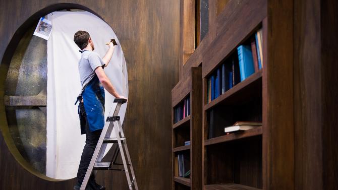 Student on ladder painting a set of a theatrical production. 