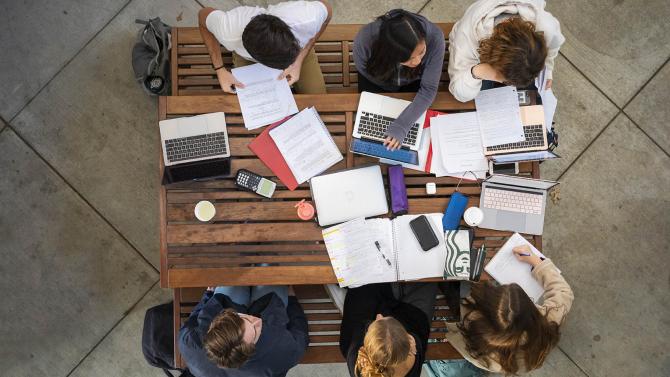 Students sit at a picnic table studying (shot is taken from above). 